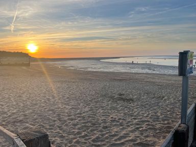 A sandy beach at sunset with people near the water and a signpost at Jolly Sailors Retreat - Wells next the Sea in Wells-Next-The-Sea