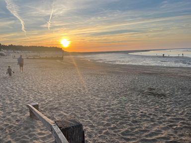 A beach at sunset with people walking near the water and sand dunes with wooden structures at Jolly Sailors Retreat - Wells next the Sea in Wells-Next-The-Sea