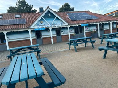 An outdoor seating area with blue picnic tables in front of a building with solar panels and signs reading beach cafe exit only and entrance at Jolly Sailors Retreat - Wells next the Sea in Wells-Next-The-Sea