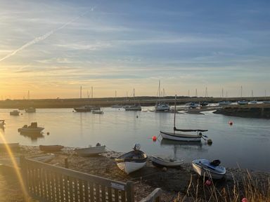A river or harbor at sunset with several boats anchored on the water and moored on the muddy shore at Jolly Sailors Retreat - Wells next the Sea in Wells-Next-The-Sea