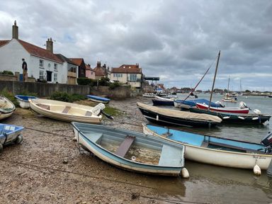 Small boats on a muddy shore with houses and a person in the background at Jolly Sailors Retreat - Wells next the Sea in Wells-Next-The-Sea