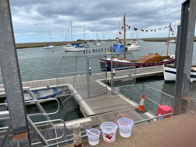 A dock area with a metal gate labeled Tug Boat Yard and several boats in the water at Jolly Sailors Retreat - Wells next the Sea in Wells-Next-The-Sea