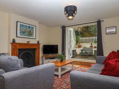 A living room with gray sofas a coffee table a fireplace and a television with an open door to a patio outside at Mimosa in Dawlish