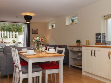 A dining table set with bowls and glasses next to a kitchen with a sink and cabinets and a living area with a sofa at Mimosa in Dawlish