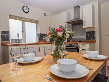 A kitchen with a wooden dining table set with bowls glasses cutlery and a vase of flowers at Mimosa in Dawlish