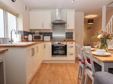A kitchen with white cabinets wooden countertops and dining table set with flowers at Mimosa in Dawlish