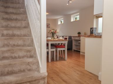 A carpeted staircase next to a dining area with a table, chairs, and a flower vase with a kitchen in the background at Mimosa in Dawlish