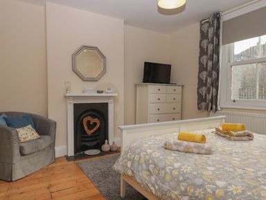 A bedroom with a bed a dresser a chair a fireplace and a window at Mimosa in Dawlish