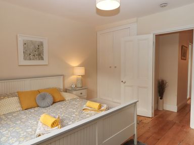 A bedroom with a bed and bedside table with lamp and an open door showing hallway at Mimosa in Dawlish