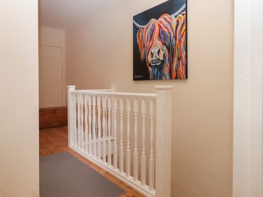 A hallway with wooden floor and white railing with a colorful painting of a cow on the wall at Mimosa in Dawlish