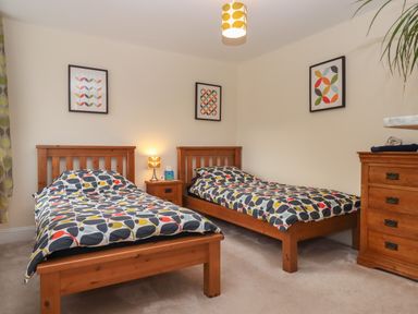 A bedroom with two single wooden beds a nightstand lamp wooden dresser and framed artwork on walls at Mimosa in Dawlish
