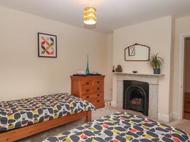 A bedroom with two single beds a wooden chest of drawers a fireplace with a mirror and a plant on the mantel at Mimosa in Dawlish