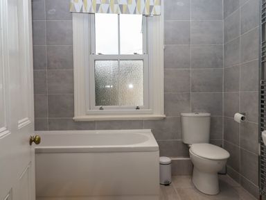 A bathroom with a bathtub toilet window and small trash bin at Mimosa in Dawlish