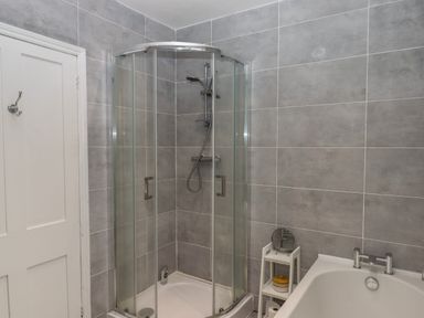 A bathroom with a corner glass shower enclosure white bathtub and a small white shelving unit at Mimosa in Dawlish