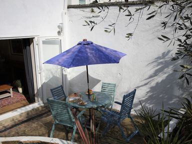 An outdoor patio with a round table and four chairs under a blue umbrella at Mimosa in Dawlish