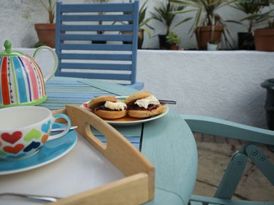 A blue wooden outdoor table and chair with scones on a plate and a teapot and cup on a tray in a garden setting at Mimosa in Dawlish