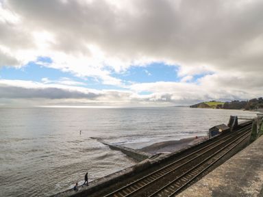 A coastal scene with railway tracks running alongside the ocean and a few people walking near the shore at Mimosa in Dawlish