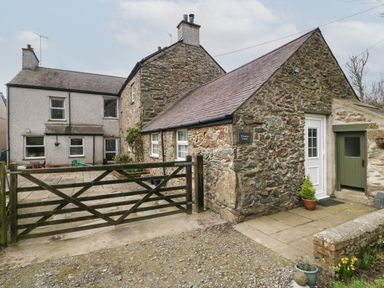 A stone cottage with a wooden gate and paved area at Ty Gwenyn in Rhydwyn