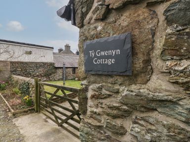 A stone wall with a sign that says Ty Gwenyn Cottage and a wooden gate leading to a garden at Ty Gwenyn in Rhydwyn
