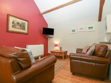 A living room with brown leather sofas a wooden coffee table a small lamp and a wall mounted television at Ty Gwenyn in Rhydwyn