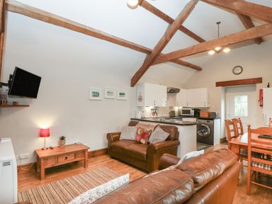 A living area with leather sofas a wooden coffee table a wall-mounted television and an open kitchen with dining table and chairs at Ty Gwenyn in Rhydwyn