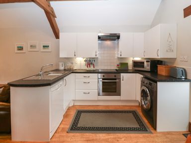 A kitchen with white cabinets black countertops a sink dishwasher oven washing machine microwave toaster and three framed pictures on wall at Ty Gwenyn in Rhydwyn
