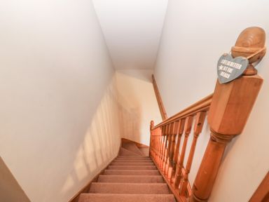 A carpeted staircase with wooden handrail and balusters in a narrow hallway at Ty Gwenyn in Rhydwyn