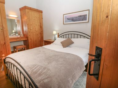 A bedroom with a bed a wooden wardrobe dressing table and a lamp at Ty Gwenyn in Rhydwyn