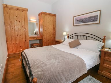 A bedroom with a double bed two wooden wardrobes bedside tables and a framed picture at Ty Gwenyn in Rhydwyn