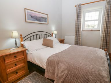 A bedroom with a double bed bedside tables with lamps a window and curtains at Ty Gwenyn in Rhydwyn