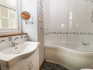 A bathroom with a sink in a cabinet a curved bathtub and a small wall mirror at Ty Gwenyn in Rhydwyn