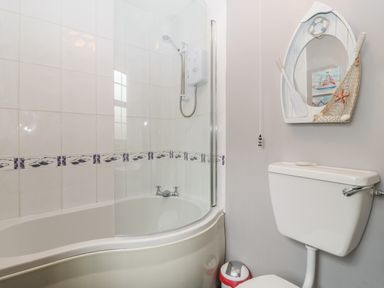 A bathroom with a bathtub shower combination and a toilet with a boat-shaped mirror above at Ty Gwenyn in Rhydwyn