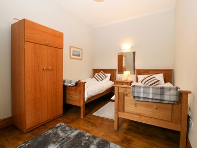 A bedroom with two single wooden beds a wardrobe a bedside table with a lamp and a mirror at Ty Gwenyn in Rhydwyn