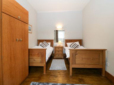 A bedroom with two wooden single beds a wooden wardrobe and a nightstand with a lamp at Ty Gwenyn in Rhydwyn