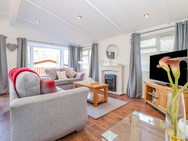 A living room with gray sofas a wooden coffee table a fireplace a television and large windows at Fell Foot Lodge Fellside 9 Limefitt Park near Troutbeck