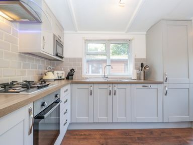 A kitchen with gray cabinets a gas stove an oven a microwave a kettle a toaster and a window at Fell Foot Lodge Fellside 9 Limefitt Park near Troutbeck
