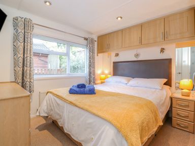 A bedroom with a bed a window curtains bedside tables lamps and wooden cabinets above the bed at Fell Foot Lodge Fellside 9 Limefitt Park near Troutbeck