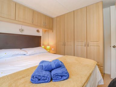 A bedroom with a double bed folded blue towels on a yellow blanket built in wooden wardrobes and cabinets at Fell Foot Lodge Fellside 9 Limefitt Park near Troutbeck
