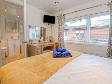 A bedroom with a bed a vanity desk with mirror and a wall mounted television at Fell Foot Lodge Fellside 9 Limefitt Park near Troutbeck