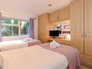 A bedroom with two single beds a window with curtains wardrobes and a small television at Fell Foot Lodge Fellside 9 Limefitt Park near Troutbeck