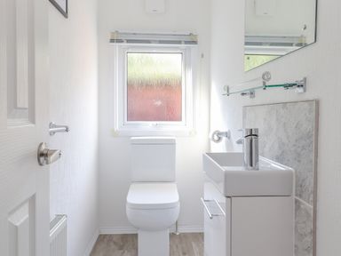A small bathroom with a toilet, a sink with a faucet, a mirror, and a frosted window at Fell Foot Lodge Fellside 9 Limefitt Park near Troutbeck