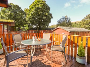 An outdoor wooden deck with a round glass table and four chairs surrounded by wooden railings at Fell Foot Lodge Fellside 9 Limefitt Park near Troutbeck