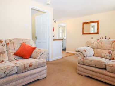 A living room with two floral patterned sofas and an orange cushion with a mirror on the wall at Little Rowan at Rowan Park Farm in Ashwater