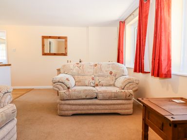 A living room with patterned armchairs red curtains wooden table and wall mirror at Little Rowan at Rowan Park Farm in Ashwater