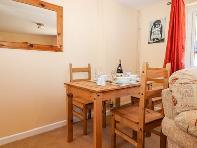 A dining area with a wooden table set with plates glasses and a bottle of wine next to a sofa and a window with red curtains at Little Rowan at Rowan Park Farm in Ashwater