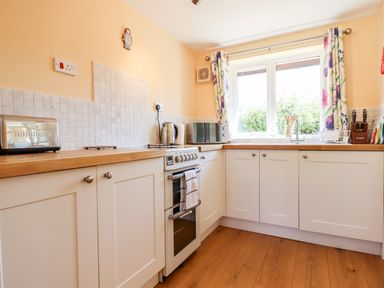 A kitchen with white cabinets wooden countertops a stove toaster kettle microwave and window with floral curtains at Little Rowan at Rowan Park Farm Ashwater