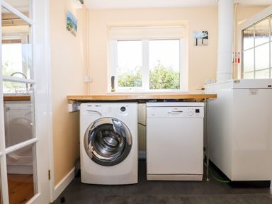 A utility room with a washing machine dishwasher and boiler under a wooden countertop with a window above at Little Rowan at Rowan Park Farm Ashwater