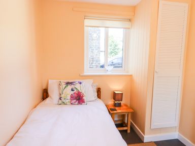 A small bedroom with a single bed white bedding floral pillow wooden nightstand and a window at Little Rowan at Rowan Park Farm in Ashwater
