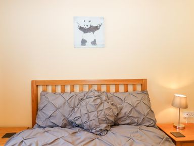 A wooden bed with gray bedding and pillows under a panda painting with two bedside tables and a lamp at Little Rowan at Rowan Park Farm in Ashwater