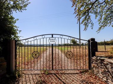 A metal gate with the words Rowan Park overlooking a gravel driveway and fields at Little Rowan at Rowan Park Farm in Ashwater